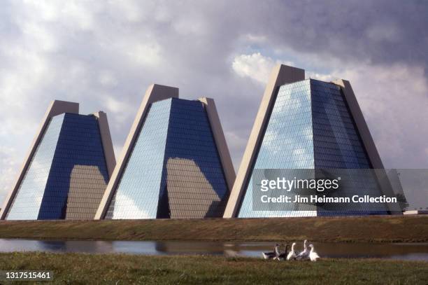 35mm film photo shows three modern office buildings in the shape of pyramids sitting adjacent to a small stream where ducks have gathered, 1987.