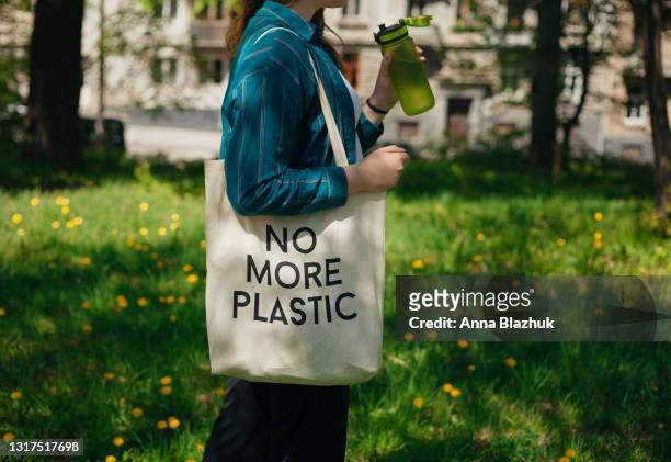 woman holding reusable cotton zero waste bag with text no more plastic. outdoors portrait in sunny day. eco friendly bags concept. - woman carrying tote bag fotografías e imágenes de stock
