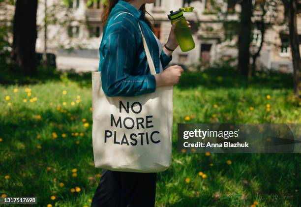 woman holding reusable cotton zero waste bag with text no more plastic. outdoors portrait in sunny day. eco friendly bags concept. - risorse sostenibili foto e immagini stock