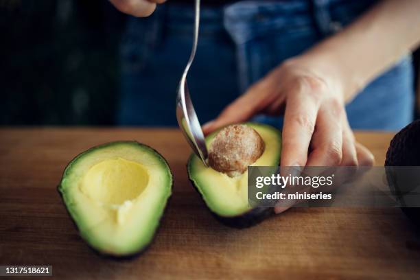 nahaufnahme foto von frau entfernen samen von avocado hälfte mit löffel - spoon in hand stock-fotos und bilder