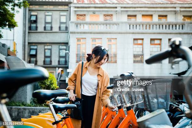 woman unlocking bicycle at rack in city - bike sharing stock pictures, royalty-free photos & images