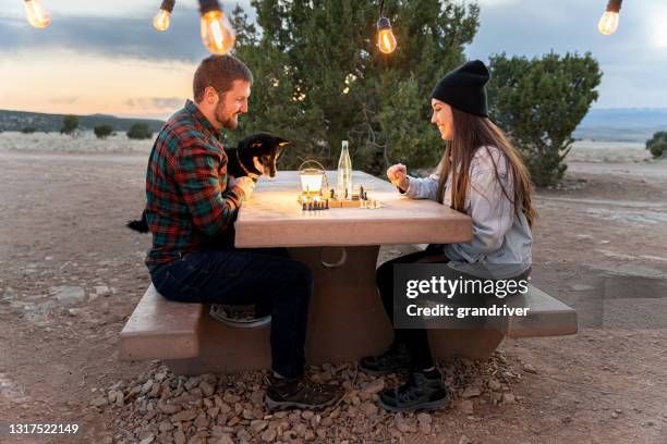 young couple camping for the weekend playing chess together at a picnic table with their dog as the sun sets - shiba inu lights 個照片及圖片檔