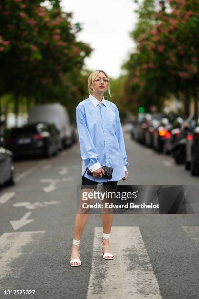 Emy Venturini @sustainably_by_emy wears glasses from Ray Ban, large earrings, a pale pastel blue long shirt with white collar from Burberry, black...