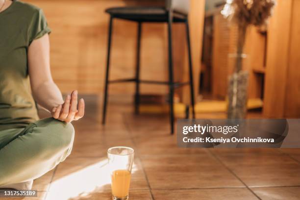 middle aged woman sitting in lotus position on a carpet in his living room. her eyes are closed. she is in the foreground, the focus is on it. in the background, the garden is blur - content stock pictures, royalty-free photos & images