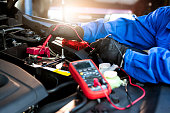 Technician uses multimeter voltmeter to check voltage level in car battery. Service and Maintenance car battery.