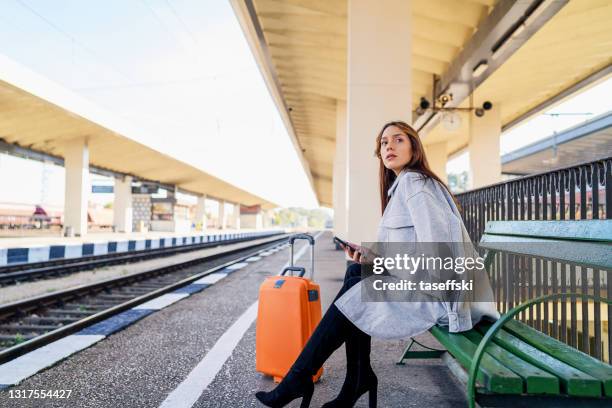 junge frau wartet auf station und mit smartphone - auf die uhr schauen stock-fotos und bilder