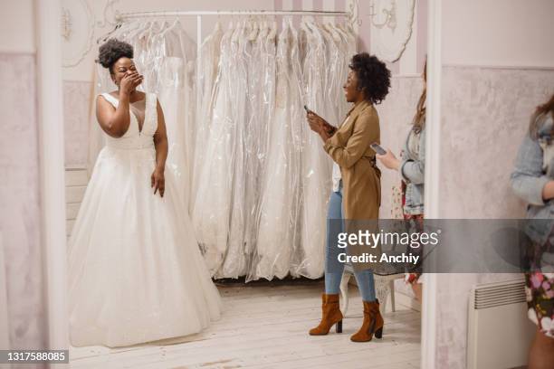 kvinna som försöker på bröllopsklänning med kvinnliga vänner som har kul och tar fotografier. - brudklänning bildbanksfoton och bilder