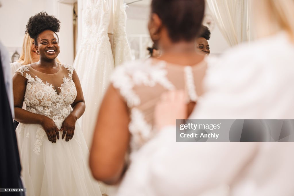 Shop assistant che aiuta la sposa a entrare nell'abito da sposa