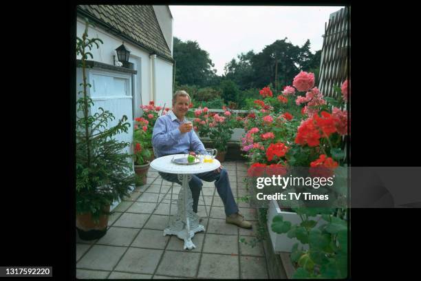 Radio and television presenter Nicholas Parsons photographed at home in his garden, circa 1983.