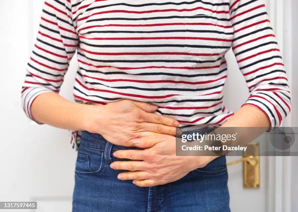 woman in pain, hands rubbing lower body for relief - ghiandola intestinale foto e immagini stock