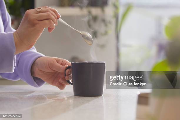 close up of hands holding spoon after stirring a hot drink in a mug - hot drink stock pictures, royalty-free photos & images
