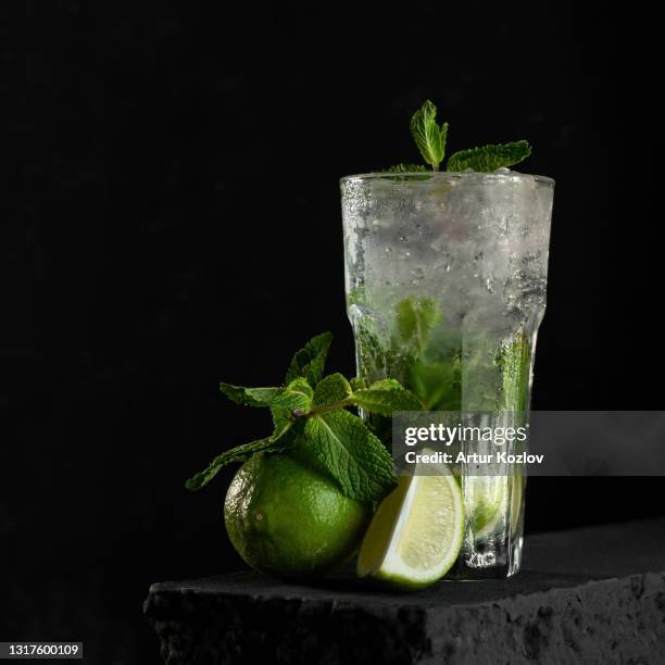 refreshing mojito. fresh lime citrus juice or soft drink with ice and mint leaves. glass with dietary vitamin product on black background. organic antioxidant cocktail. copy space - モヒート ストックフォトと画像