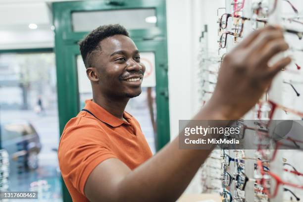 young african american man choosing the eyeglasses at the optics store - choosing eyeglasses stock pictures, royalty-free photos & images