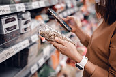 Woman shopping in supermarket and reading product information. Costumer buying food at the market.