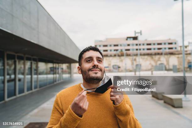 el hombre millennial está respirando profundamente al aire libre mientras se quita la máscara protectora de la cara - removing fotografías e imágenes de stock