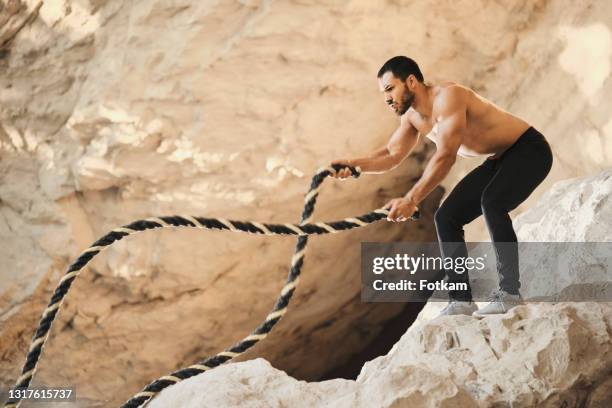 a young male athlete is doing exercises with a battle rope. surrounded by nature and rocks. - battle rope stock pictures, royalty-free photos & images