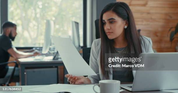 shot of a young businesswoman sitting at her desk reading some documents in her office - stern form stock pictures, royalty-free photos & images