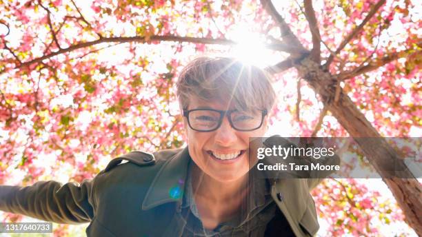 woman smiling at camera under cherry blossom tree - blossom tree stockfoto's en -beelden