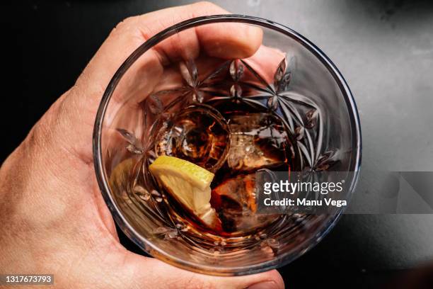 top view hand of a man holding of a whiskey cocktail on ice with lemon on glass - old fashioned glass stock pictures, royalty-free photos & images