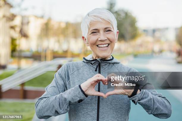 glimlachende hogere vrouw die een hartteken met haar handen maakt - hand with hart stockfoto's en -beelden