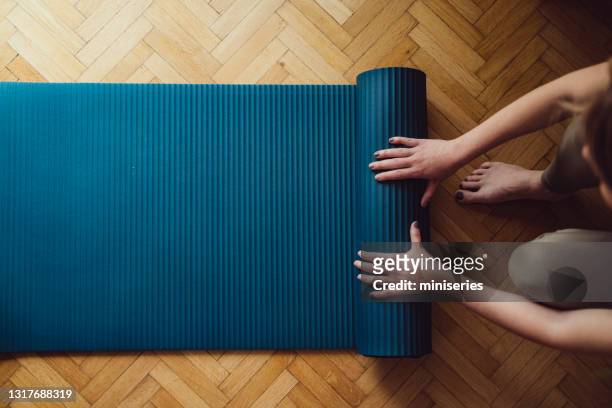 fermez-vous vers le haut des mains femelles pliant le tapis bleu d’exercice sur le plancher en bois - salle yoga photos et images de collection