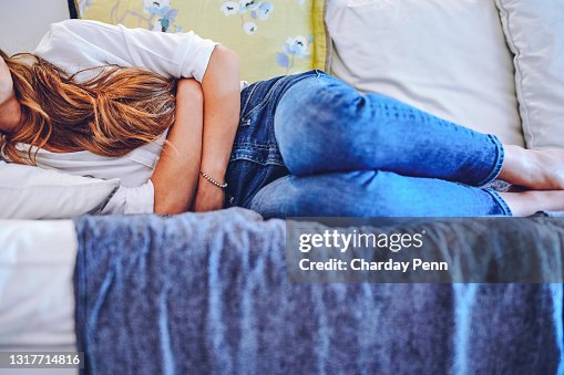 Schuss einer nicht wiederzuerkennenden Frau, die Bauchschmerzen beim Liegen auf dem Sofa zu Hause hat Schuss einer nicht wiederzuerkennenden Frau, die Bauchschmerzen beim Liegen auf dem Sofa zu Hause hat