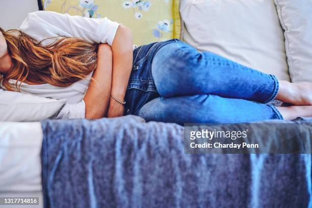 shot of an unrecognisable woman experiencing stomach pain while lying on the sofa at home - stomach stock pictures, royalty-free photos & images