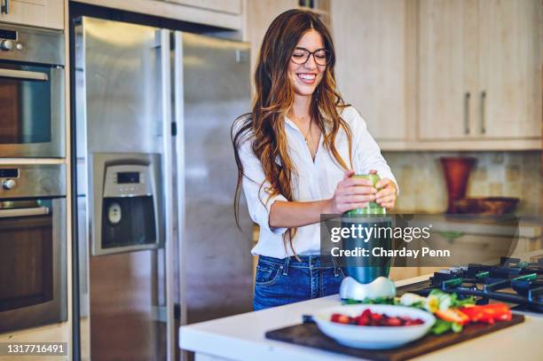 ontsproten van een jonge vrouw die een gezonde smoothie thuis maakt - smoothie and woman stockfoto's en -beelden