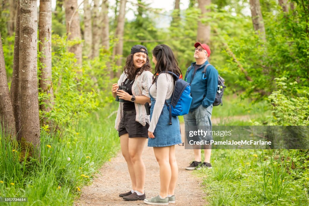 Sisters Laughing While Walking and Birdwatching in Forest with Father