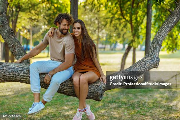 ein junges paar sitzt auf einem zweig in der natur. - woman smiling park summer stock-fotos und bilder
