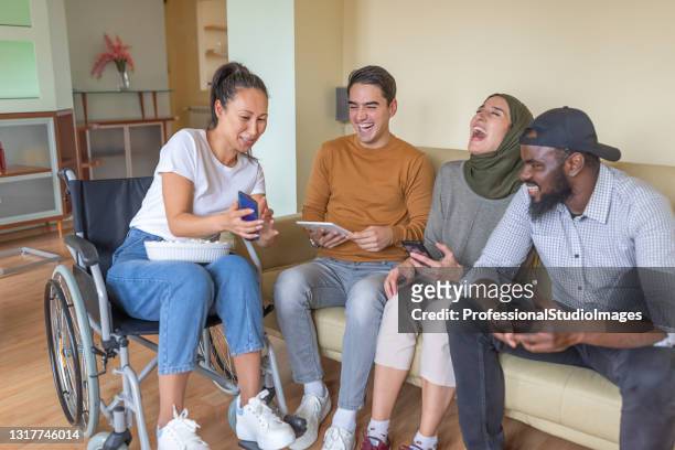 a happy multi-ethnic group of young friends is having fun at home using tablet and phones. - disability collection stock pictures, royalty-free photos & images