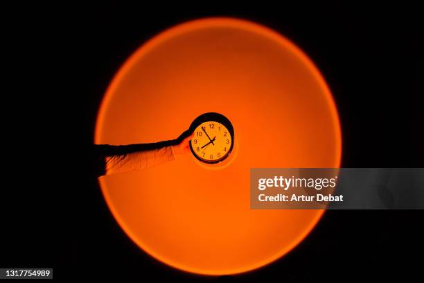 holding wall clock against big sunset sun light effect. - zeitstrahl stock-fotos und bilder
