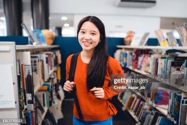 smiling young student in a library. - glowing book stock pictures, royalty-free photos & images