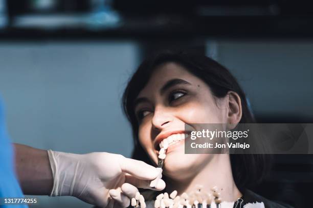 un dentista utiliza varias piezas de un molde dental para ver cuál se adapta mejor a los dientes de una paciente. - paciente stock pictures, royalty-free photos & images