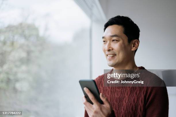 sorridente uomo dell'asia orientale che usa lo smartphone a casa - popolazione dellasia orientale foto e immagini stock