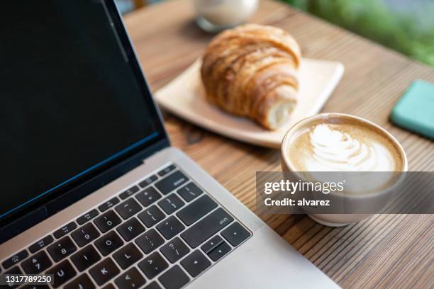 ラップトップコンピュータとカフェテーブルのクロワッサン付きラテアートコーヒー - latte art ストックフォトと画像