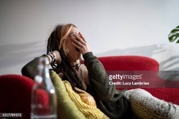 young woman with a unique style, yawning and relaxing on a red sofa - tired stockfoto's en -beelden