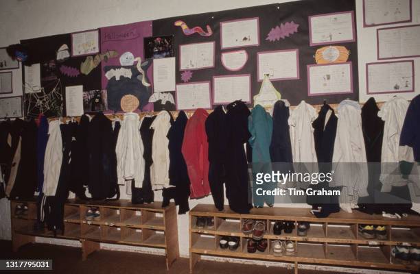 Kits hanging in the changing room, footwear in a rack below, with Halloween-themed schoolwork pinned to the wall above the clothes hooks, in a scene...