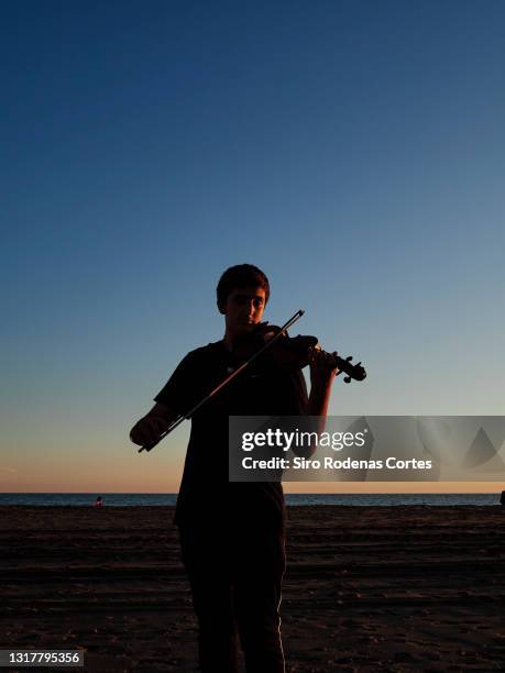 silhouette of boy playing violin at sunset on the beach - young violinist stock pictures, royalty-free photos & images