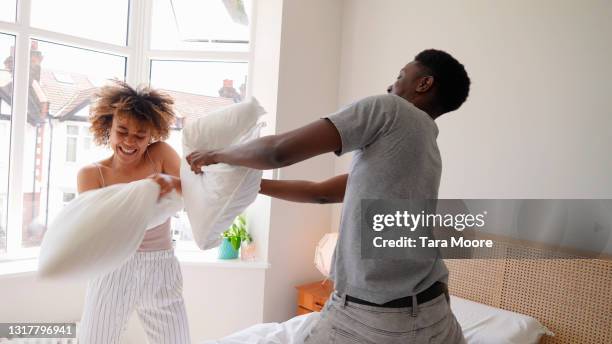 young couple having pillow fight in bedroom - pillow fight fotografías e imágenes de stock