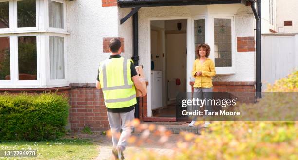 delivery man delivering parcel to young woman's house - postino foto e immagini stock