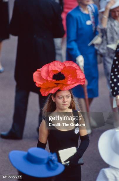 Female racegoer wearing a black dress, black evening gloves, and a red hat among the racegoers on the first day of the Royal Ascot race meeting at...
