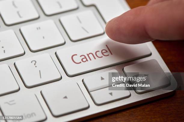 a finger about to press a "cancel" button on a computer keyboard. - cancelamento imagens e fotografias de stock