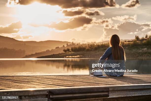 unrecognizable young woman on her back on a wooden pier of a lake with a parasol, watching the sunset. - watching sunset stock pictures, royalty-free photos & images