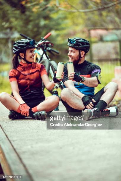 cyclist couple sharing beer while resting from journey and making celebratory toast - beer flowing stock pictures, royalty-free photos & images