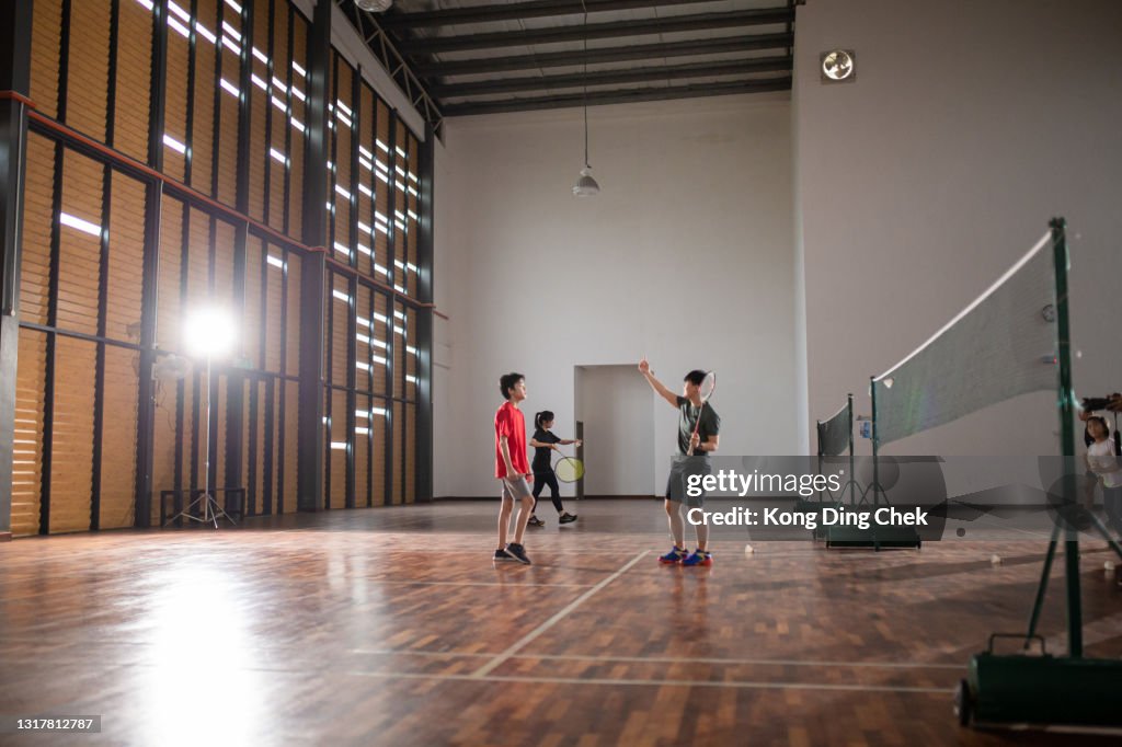 Asiatisk kinesisk kvinnlig badmintontränare som undervisar sin student i badminton domstol