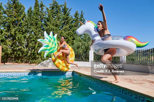 two women jumping into the pool with float - float photos et images de collection