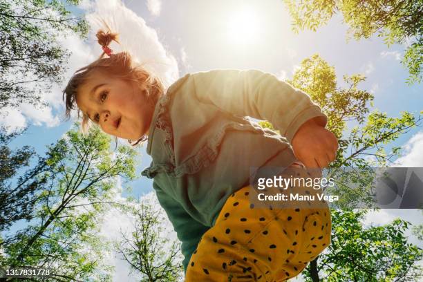 view of a little girl from below with pigtails in the park in sunny day - surprise face kid stock-fotos und bilder
