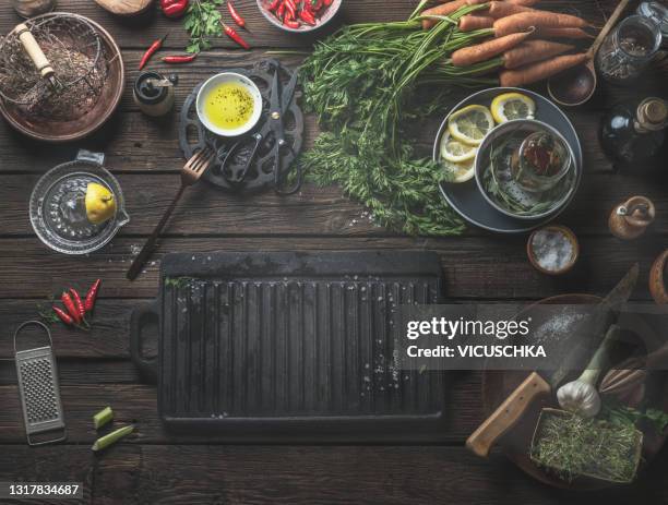 food background with empty black cast iron grill griddle with copy space, ingredients and vintage kitchen utensils on wooden kitchen table - gusseiserne pfanne stock-fotos und bilder