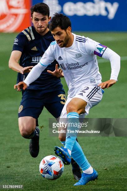 Carles Gil of the New England Revolution dribbles past Leon Flach of the Philadelphia Union during the first half at Subaru Park on May 12, 2021 in...